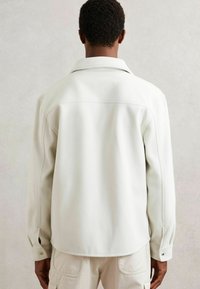 Hombre visto desde atrás que lleva una chaqueta de forro polar color crema con mangas largas y pantalones beige con bolsillos de parche.