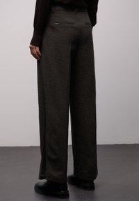 Pantaloni verde scuro a gamba larga realizzati in tessuto strutturato con motivo a spina di pesce. Dotati di tasche posteriori e una cintura liscia.