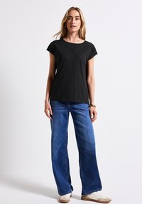 Haut noir à manches courtes avec un col rond, associé à un jean bleu ample et des baskets beiges. Design simple et décontracté.