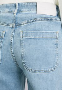 Lichtblauwe denim jeans met een slim fit, voorzien van twee achterzakken, zichtbare stiksels en een wit lederen merklabel op de tailleband.