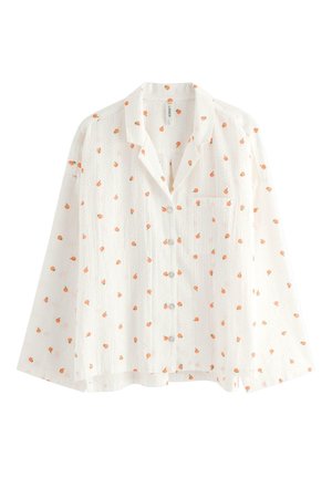 Valkoinen pitkähiha-painonappikauluspaita, jossa on pieni oranssin hedelmän kuvio ja vasemmalla puolella rintatasku.