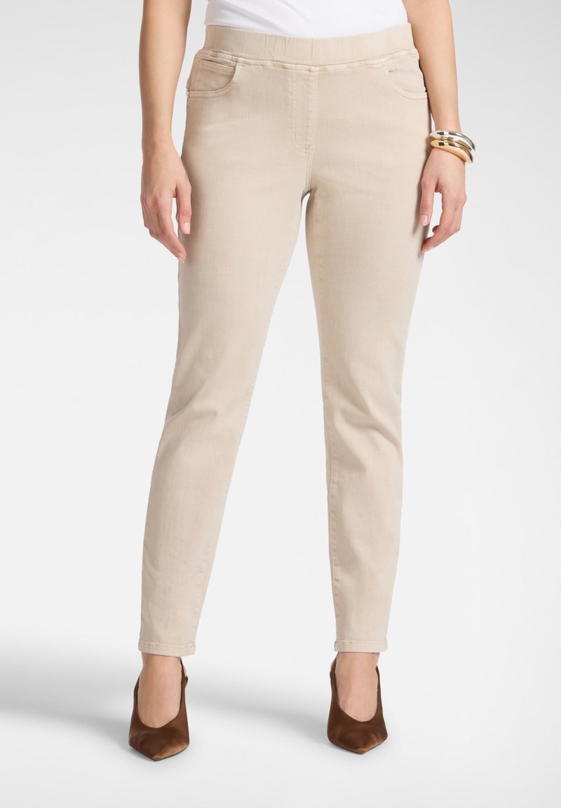 Pantalones beige de tiro alto con diseño de cinco bolsillos, pierna estrecha, textura de tela lisa y cintura elástica, combinados con tacones puntiagudos marrones.
