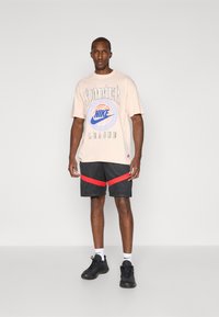 Lys ferskenfarvet t-shirt med "Summer League" og Nike-logo; sorte shorts med røde striber; sorte sko; atletiske hvide sokker.