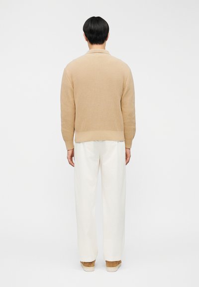 Μπεζ πλεκτό πουλόβερ με υφή, συνδυασμένο με λευκό παντελόνι φαρδιάς γραμμής και ανοιχτό καφέ παπούτσια, σε άποψη από πίσω.