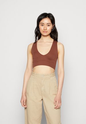 Top cropped castanho com decote em V profundo, combinado com calças de cintura alta em bege claro. Tecido suave com um design justo.