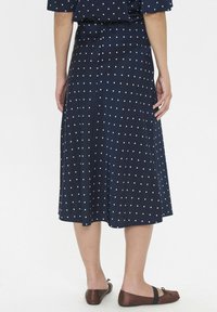 Jupe bleu marine à pois, fabriquée en tissu doux, avec une silhouette évasée qui atteint le milieu du mollet, et des ballerines marron visibles en dessous.