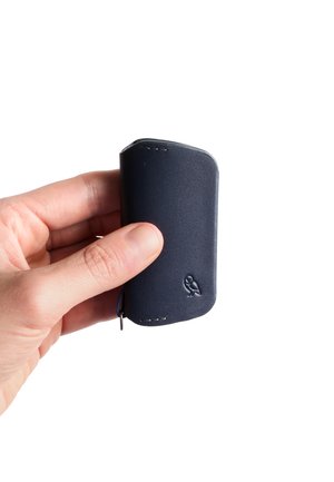 Navy leather cardholder with rounded edges, visible stitching, and embossed owl logo. Compact shape, held in a hand.