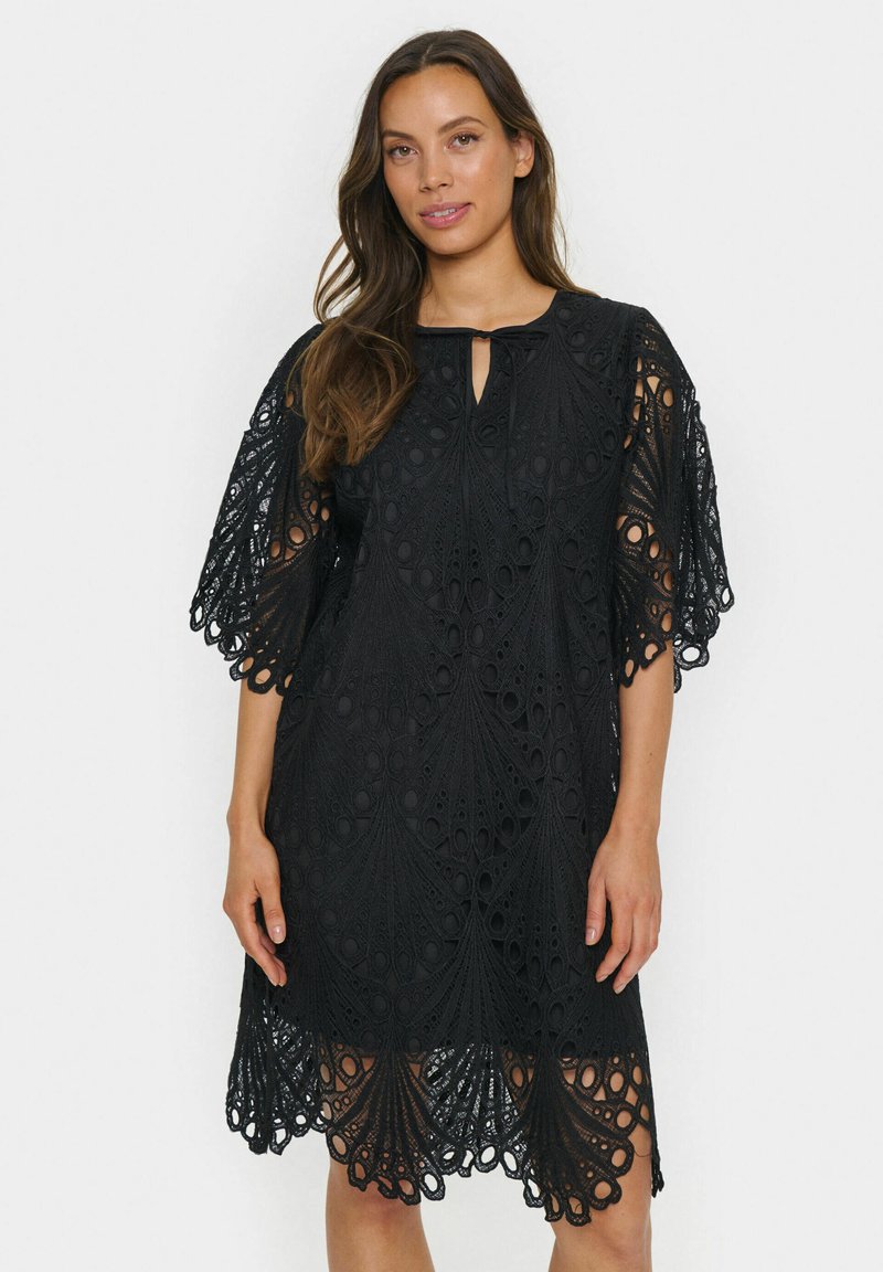 Black lace dress with intricate circular cutouts and a scalloped hem. Features short, fluttering sleeves and a keyhole neckline design.
