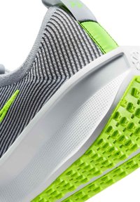 Zapatilla atlética gris con parte superior a rayas, entresuela blanca y suela texturizada de un verde brillante; cuenta con un tirador y acentos reflectantes.