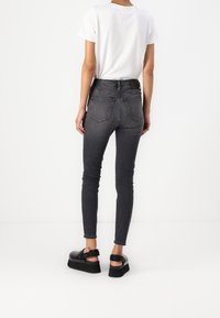 Slim fit-jeans i mörkgrå denim med en slät yta, med en medelhög midja och två bakfickor. Bärs med en vit T-shirt och svarta sandaler.