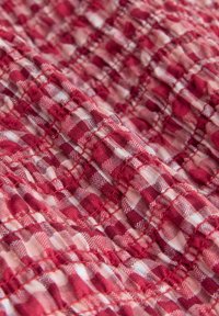 Material în carouri roșii și roz, cu o suprafață texturată, având pătrate mici și detalii de cusături strânse pe toată suprafața.