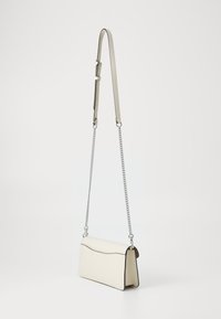 Krämfärgad läder crossbody-väska med silverkedja och strap av konstläder, med en rundad topp och kontrasterande mörka detaljer.