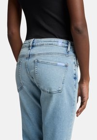 Jeans in denim blu chiaro con cinque tasche, una vita standard e un piccolo etichetta blu sul retro. Tessuto liscio, vestibilità rilassata.