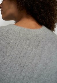 Pull gris en maille avec une finition douce et texturée. Il présente un col large et un petit logo "10" cousu à l'arrière.