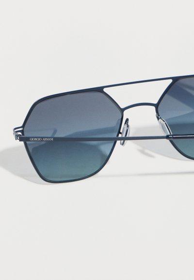 Κομψά γυαλιά ηλίου Giorgio Armani με σκούρους μπλε γεωμετρικούς φακούς και λεπτό μεταλλικό πλαίσιο σε λευκό φόντο.