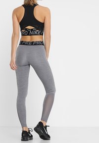 Zwarte sportieve crop top met een uitgesneden rug, gecombineerd met grijze leggings met een gladde textuur en mesh-panelen langs de benen.