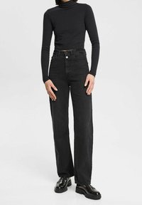 Jeans negros de cintura alta con corte recto, que cuentan con un clásico cierre de botón y diseño de cinco bolsillos, combinados con un ajustado suéter negro de cuello cisne.