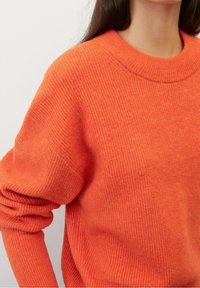 Pletený oranžový svetr s kulatým výstřihem, žebrovanou texturou a mírně oversize střihem s ohrnutými rukávy a hladkým povrchem.