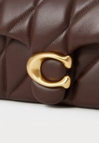 Brown quilted leather handbag featuring a prominent gold-toned C-shaped clasp and smooth texture with fine stitching details.