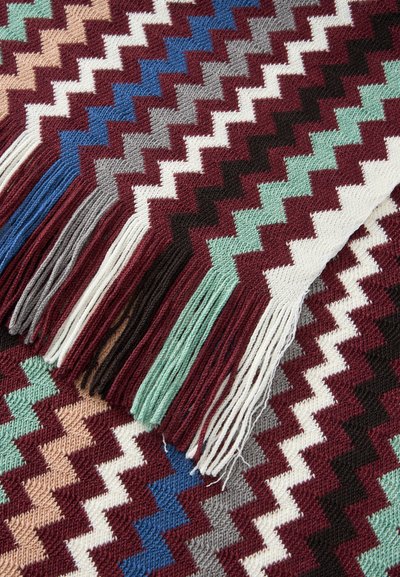 Tissu tricoté avec des motifs en zigzag multicolores et des franges dans des teintes bordeaux, bleu, gris, vert, blanc et beige.