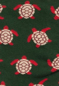 Stricksocken mit einem grünen Hintergrund und sich wiederholenden Schildkrötenmustern in Creme und Rot, die detaillierte Panzer- und Flossendetails zeigen.