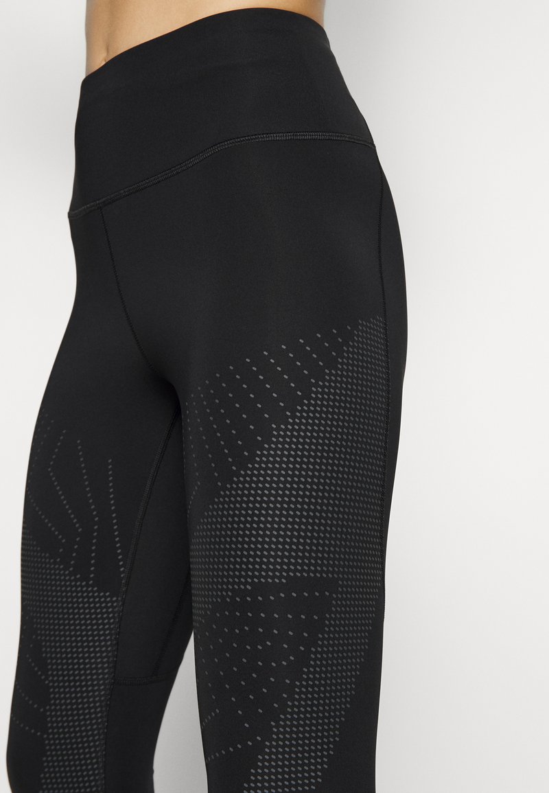 Zwarte hoge taille leggings gemaakt van rekbaar materiaal. Heeft subtiele stippenpatronen aan de zijkanten en een gladde textuur.
