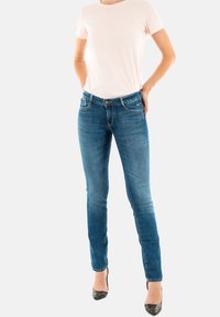 T-shirt ajusté rose clair associé à un jean skinny bleu foncé avec un léger effet délavé, un design à cinq poches et des accents métalliques. Talons noirs.