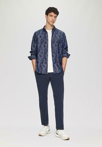 Navy gestreepte lange mouw shirt over een witte t-shirt, gecombineerd met navy broek en witte sneakers. Het shirt heeft een subtiel ontwerp.