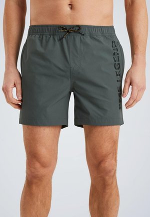 Donkergroene zwembroek met een elastische tailleband en trekkoord. Heeft een zwart logo dat verticaal aan de zijkant is gedrukt. Lichtgewicht materiaal.