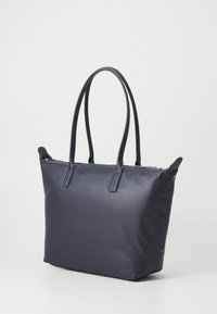 Marine tote bag laget av glatt syntetisk materiale, med to lange håndtak og glidelås, og en subtil logo detalj på siden.