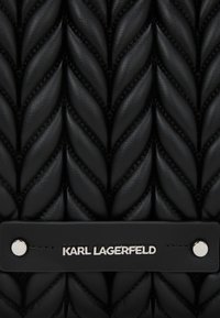 Sac en cuir noir avec un motif matelassé ressemblant à un tissu tordu. Présente une surface texturée et un accent logo argenté.