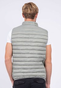 Gilet rembourré gris clair avec des sections matelassées horizontales, un col montant et des emmanchures. Le design du dos est lisse et minimaliste.