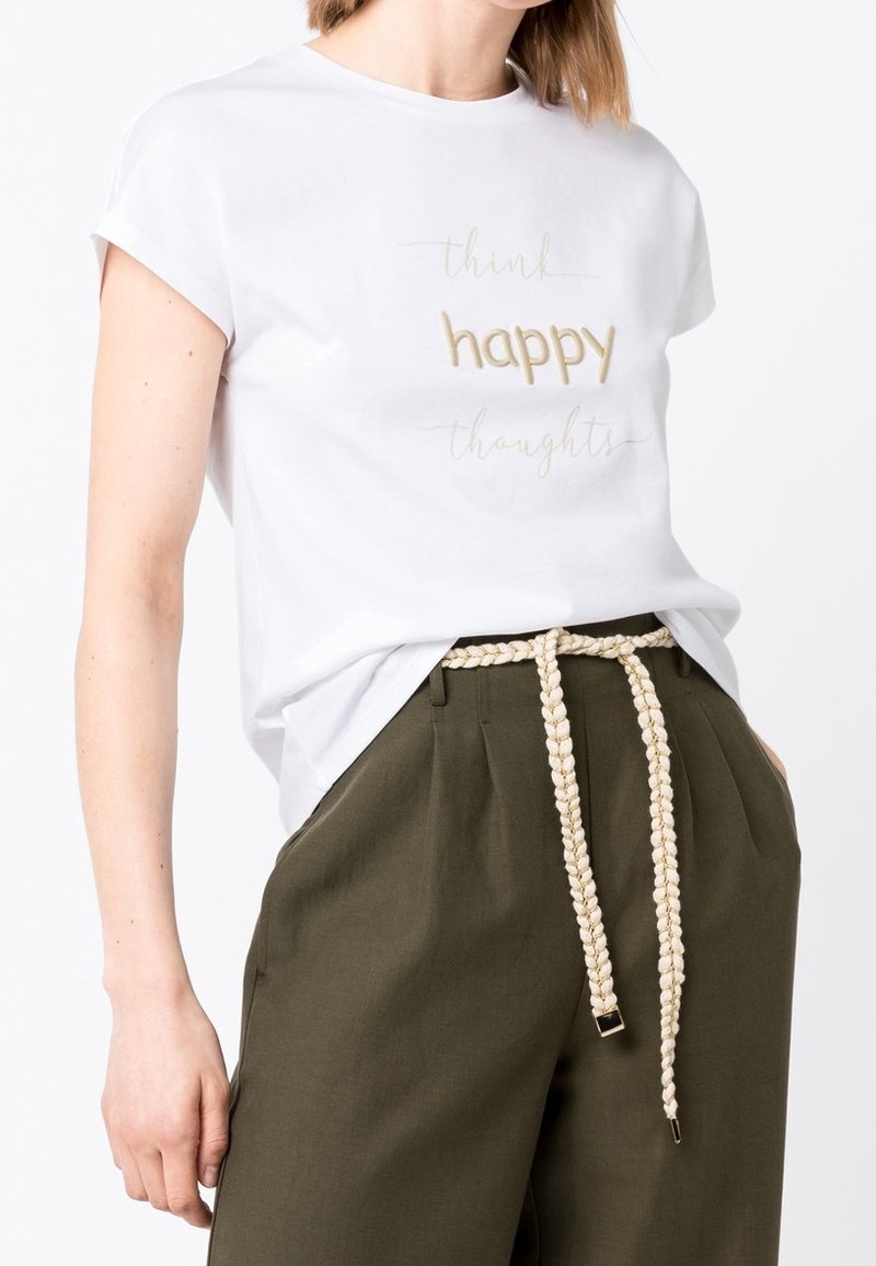 Weißes Baumwoll-T-Shirt mit aufgerollten Ärmeln, mit metallic-goldfarbenem Text: "denke positive Gedanken." Olivgrüne, hoch taillierte Hose mit geflochtenem Gürtel.