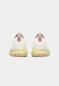 White sneakers with pale pink accents and a yellow sole. Features a textured upper, padded collar, and distinct pull tab at the back.