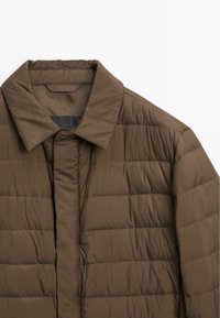Quilted brun pufferjakke med spredt krave og lodrette syninger. Materialet virker let og vandafvisende.