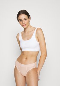 Sujeción deportiva blanca con tirantes anchos y un logo sutil; combinada con braguitas seamless de color rosa claro con una cinturilla ancha y un acento de logo.