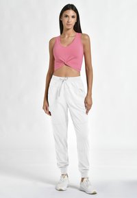 Rosa kort tanktop med snoet frontdesign, parret med løstsiddende, hvide joggerbukser med elastisk talje og sidelommer.