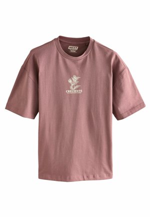 Roserosa bomulds t-shirt med rund hals og korte ærmer. Har et hvidt blomstermotiv og teksten "CRECIENTE EL CAMPO DE FLORES."
