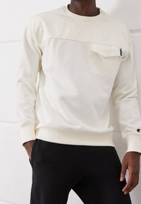 Felpa bianca con scollo rotondo, tasca frontale e polsini a costine, caratterizzata da un piccolo logo del marchio sulla manica e una finitura liscia e testurizzata.