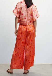 Bloemrijke blouse en brede broek in tinten van roze en oranje, gemaakt van lichtgewicht stof, met een relaxte pasvorm en korte mouwen.