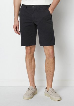 Marineblå bomullsshorts med rett passform, med to frontlommer og knappelukking i midjen. Brukt sammen med lysegrå sko.