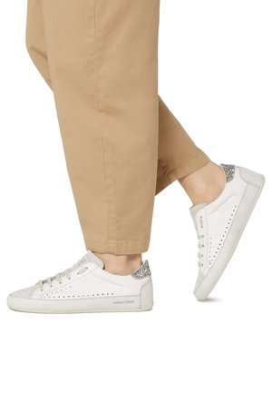 White leather sneakers with a textured silver accent on the heel, featuring perforations on the outer side and beige laces.