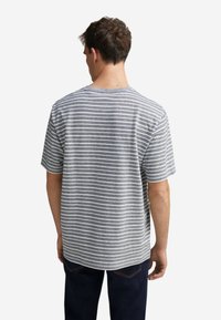 Šedé a bílé pruhované tričko s krátkým rukávem a kulatým výstřihem, s volným střihem a měkkou strukturou, oblečené s tmavými džíny.