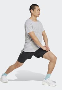 Šedé pruhované tričko s krátkym rukávom, čierne šortky, biele tenisky a svetlomodré ponožky; mužská postava v polohe výpadu.