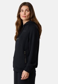 Mustat hupparitakki, joka on valmistettu pehmeästä kankaasta. Varustettu vetoketjullisilla taskuilla, joissa on kultaiset yksityiskohdat ja ribbireunus. Minimalistinen muotoilu logotwistillä.
