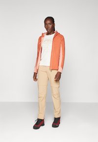 Lightweight, two-tone orange zip-up jacket, beige cargo pants, and black/red hiking boots. Cotton t-shirt with graphic design.