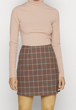 Haut à col roulé côtelé rose clair associé à une minijupe à carreaux marron avec des accents rouges et noirs et un détail de fente sur le côté.