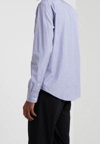 Chemise bleue clair à manches longues en tissu texturé ; avec un col et des poignets à bouton ; ourlet arrondi ; associée à un pantalon noir.