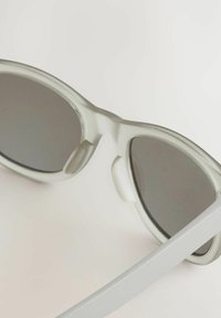Lunettes de soleil avec une monture gris clair mate, des verres gris foncé, un design aérodynamique et des embouts de branches texturés pour une meilleure prise.