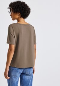 Olivově zelené tričko s krátkým rukávem vyrobené z měkké látky, s kulatým výstřihem a volným střihem, kombinované se světle modrými džíny.